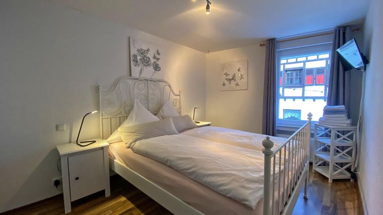 Ein gemütliches Schlafzimmer mit einem weißen Bett und hellen Wänden. Der Raum hat Holzfußboden und einen Fernseher an der Wand.