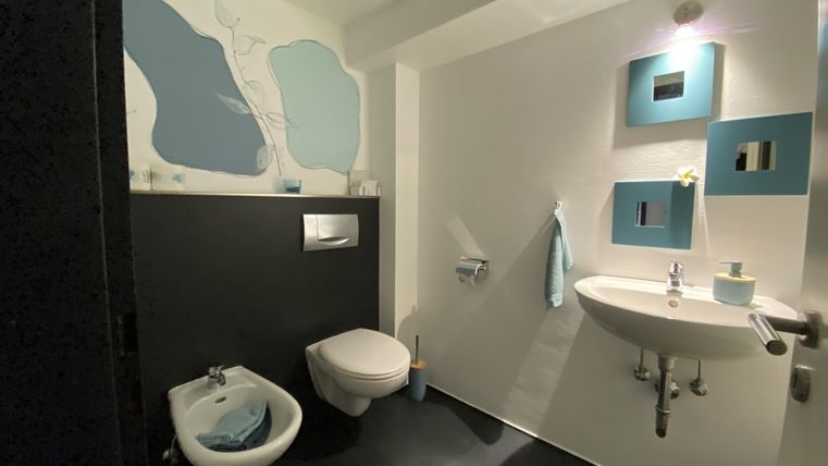 Ein modernes Badezimmer mit schwarzen und weißen Wänden sowie blauen Akzenten. Es enthält eine Toilette, ein Bidet und ein Waschbecken.
