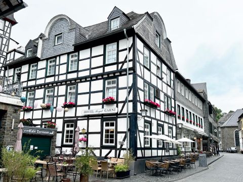 Ein historisches Fachwerkhaus mit blühenden Blumenkästen. Vor dem Gebäude befinden sich gemütliche Terrassen mit Tischen und Stühlen.