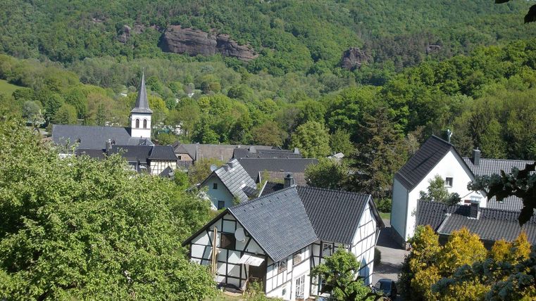 Ein malerisches Dorf umgeben von grünen Hügeln. Die schönen Fachwerkhäuser und die Kirche prägen die idyllische Landschaft.