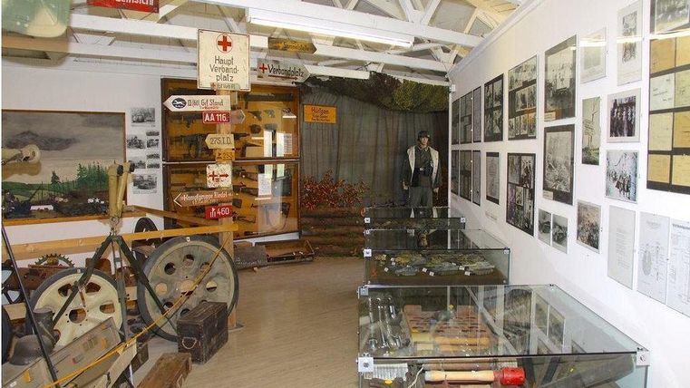 Ein Museum mit historischen Artefakten, darunter Werkzeuge und Fotografien an den Wänden. In der Mitte steht eine Statue, umgeben von Vitrinen mit verschiedenen Ausstellungsstücken.