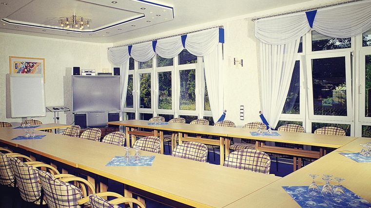 Ein moderner Konferenzraum mit einem großen Tisch und zahlreichen Stühlen. Große Fenster lassen viel Licht herein und bieten einen Blick nach draußen.
