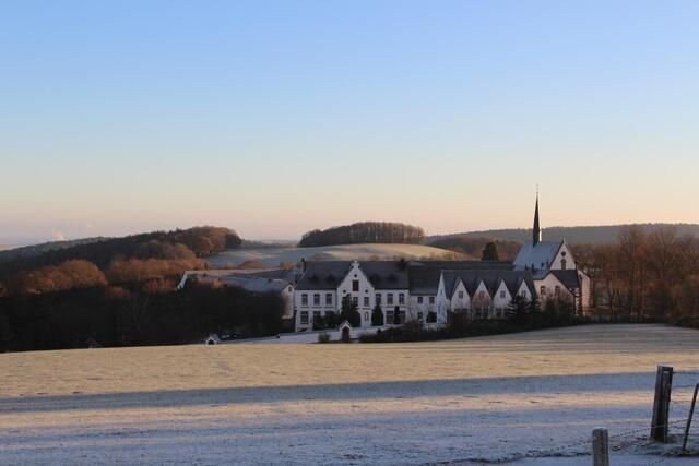 Ein malerisches Landschaftsbild mit einem historischen Gebäude im Vordergrund. Der Himmel ist klar und die Umgebung ist von leichtem Frost bedeckt.