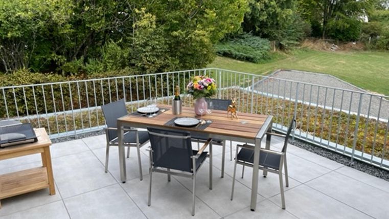 Ein einladender Balkon mit einem eleganten Tisch und Stühlen. Auf dem Tisch steht eine Blumenvase und Geschirr, umgeben von grüner Vegetation.