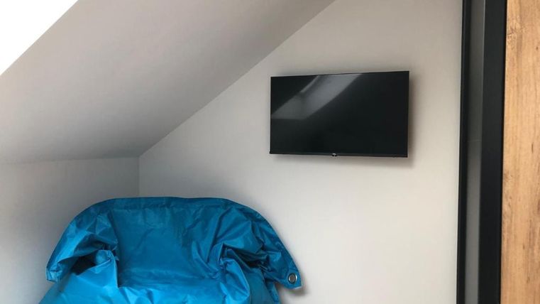 Ein gemütlicher Raum mit einem blauen Sitzsack und einem Wandfernseher. Die Wände sind hell, und der Boden ist aus Holz.