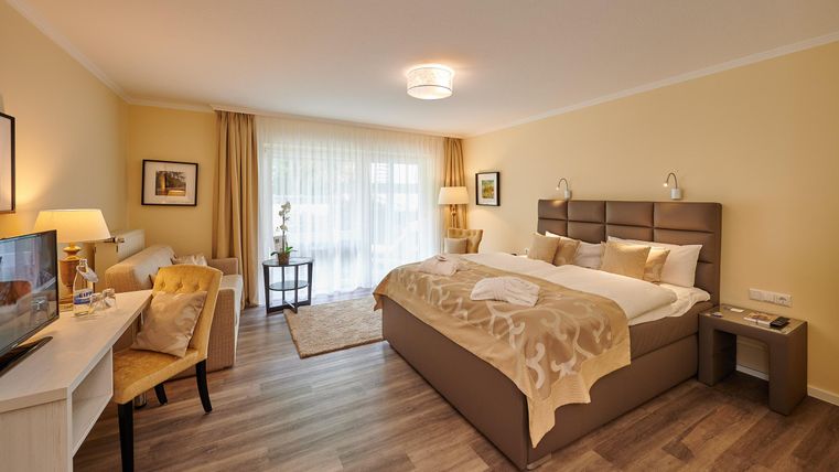Ein modernes Schlafzimmer mit einem großen Bett und einem gemütlichen Arbeitsbereich. Das Zimmer hat viel Tageslicht und ist geschmackvoll eingerichtet.
