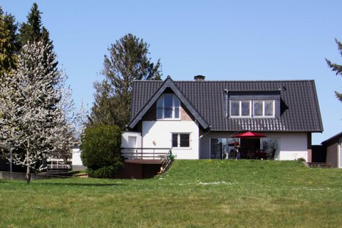 Ein modernes Haus mit einem schwarzen Dach und einem Balkon. Umgeben von grünem Rasen und Bäumen.