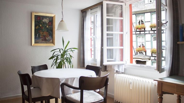 Ein gemütlicher Raum mit einem runden Tisch und schwarzen Stühlen. Das Fenster ist geöffnet und bietet einen Blick auf bunt dekorierte Fensterbänke.