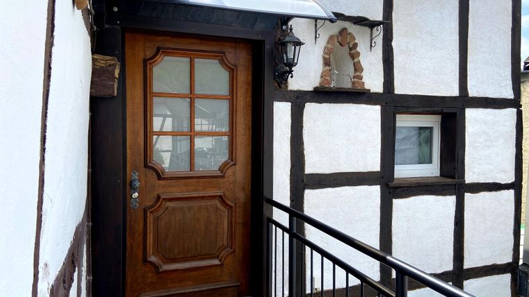Eine stilvolle Haustür aus Holz in einem Fachwerkgebäude. Die Fassade hat weiße Wände mit dunklen Balken und einen kleinen Balkon.