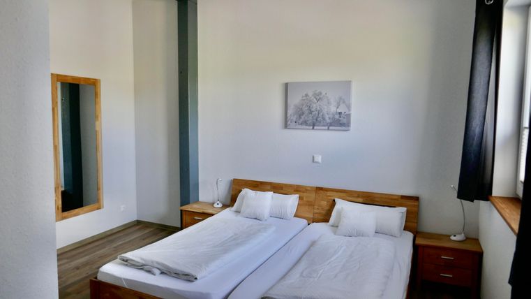 Ein helles Schlafzimmer mit zwei Einzelbetten und einem Holzschrank. An der Wand hängt ein Bild, und eine große Spiegel ist ebenfalls sichtbar.