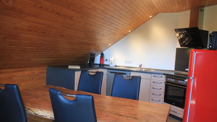 Eine moderne Küche mit Holzdecke und hellen Wänden. Der Raum verfügt über einen Esstisch aus Holz und moderne Küchengeräte.
