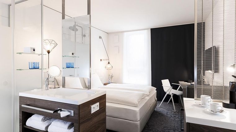 Ein modernes Hotelzimmer mit einem gemütlichen Doppelbett und eleganten Möbeln. Die helle Einrichtung und die große Fensterfront sorgen für eine freundliche Atmosphäre.