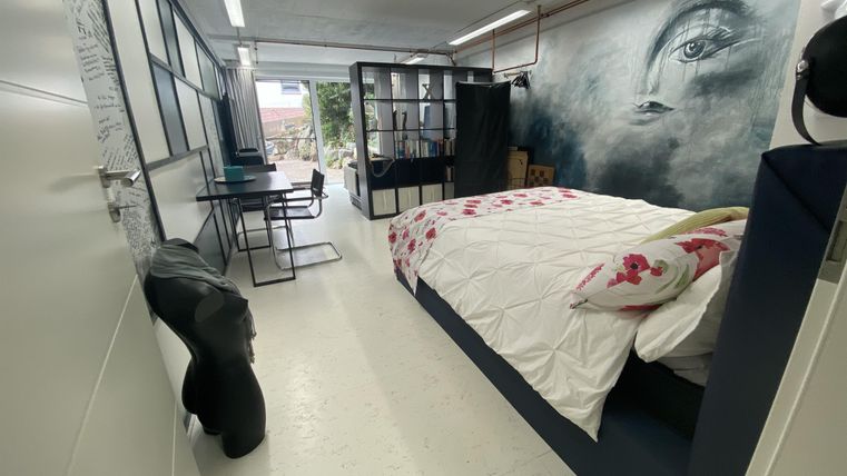 Ein modernes Zimmer mit einem großen Bett und einer Blumenbettwäsche. An der Wand befindet sich ein eindrucksvolles Wandbild, und es gibt einen kleinen Arbeitsplatz mit einem Tisch und Stuhl.