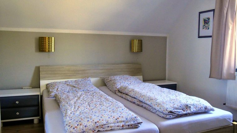 Ein gemütliches Schlafzimmer mit zwei getrennten Betten und bunten Bettdecken. An der Wand hängen zwei Lampen, und ein Nachttisch steht daneben.