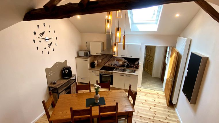 Eine moderne Küche mit einem Holztisch und Stühlen. Die Decke hat sichtbare Balken und große Fenster sorgen für viel Licht.