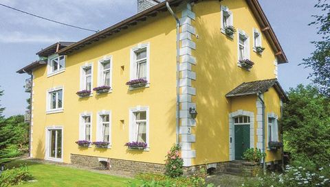 Ein schönes, gelbes Haus mit weißen Fenstern und blauen Blumenkästen. Der Garten ist gepflegt und umgeben von Grün.