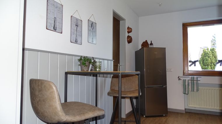 Eine moderne Küche mit einem hohen Tisch und zwei Stühlen. Die Wände sind dekoriert mit Bildern und es gibt ein Fenster mit Blick ins Freie.
