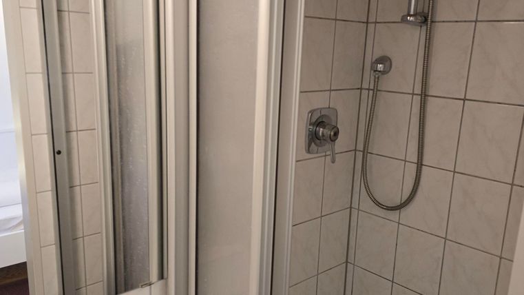 Eine moderne Dusche mit Glasabtrennung und hellen Fliesen. Neben der Dusche befindet sich ein Waschbecken.