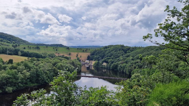 Eine malerische Landschaft mit einem Fluss und üppigem Grün. Der Himmel ist bewölkt, aber die Natur wirkt einladend.