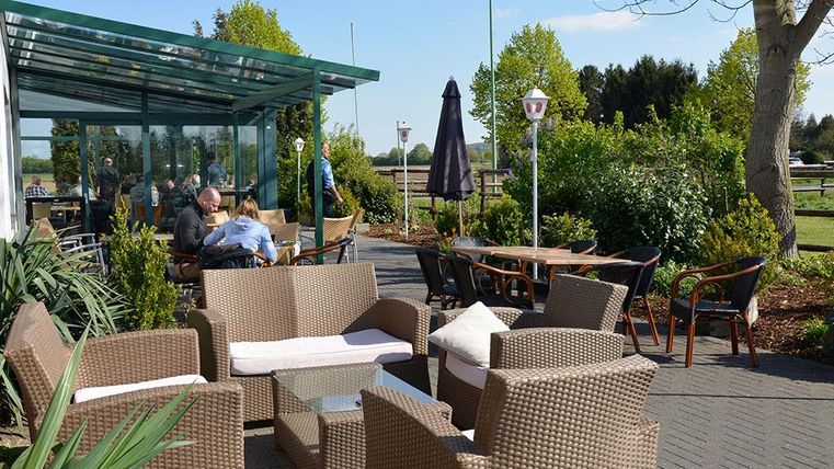 Eine gemütliche Terrasse mit Gartenmöbeln und Sonnenschirmen. Im Hintergrund sind Gäste, die die frische Luft genießen.
