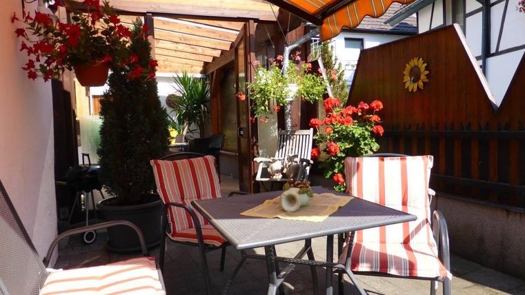 Ein gemütlicher Außenbereich mit gestreiften Stühlen und einem Tisch. Bunte Blumen und Pflanzen schaffen eine einladende Atmosphäre.