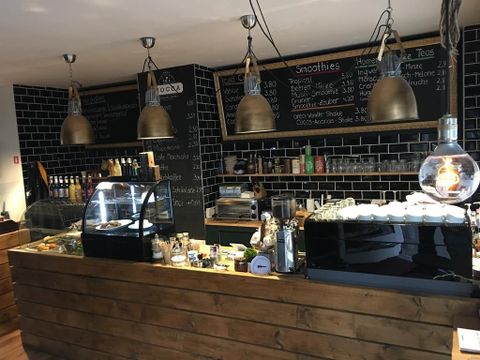 Ein gemütliches Café mit einer Holzbar und modernen Lampen. Die Wand ist mit einer Speisekarte und erfrischenden Getränken dekoriert.