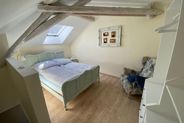 Ein gemütliches Schlafzimmer mit einem Doppelbett und Holzdecke. Es gibt einen Sessel und einen kleinen Tisch am Fenster.
