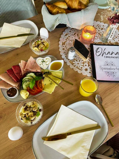 Ein ansprechend gedeckter Tisch mit verschiedenen Frühstücksgerichten. Es gibt Aufschnitt, Käse, frisches Gemüse und ein Getränk.