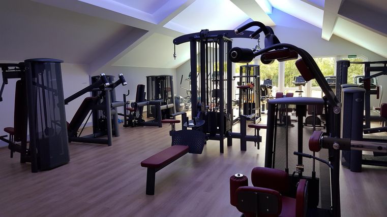 Ein modernes Fitnessstudio mit mehreren Trainingsgeräten und einem hellen, offenen Raum. Die Wände sind schattig und der Boden ist aus Holz.