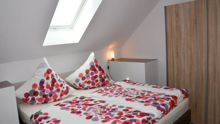 Ein gemütliches Schlafzimmer mit einem Doppelbett und bunten Kissen. Das Zimmer hat einen Dachfenster und modernen Möbeln aus Holz.
