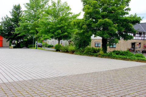 Ein leerer Platz mit einem Pflasterboden und einigen Bäumen. Im Hintergrund sind Gebäude zu sehen.