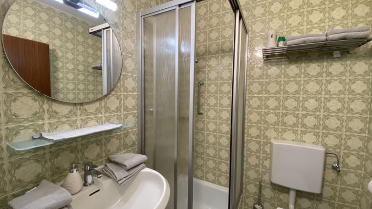 Ein kleines Badezimmer mit einer Dusche und einem Waschbecken. Die Wände sind mit einer dekorativen Tapete versehen und es gibt ein rundes Spiegel.