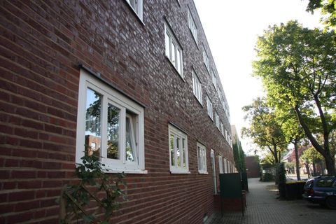 Ein mehrstöckiges Backsteingebäude mit Fenstern an der Seitenansicht. Im Vordergrund sind Bäume und ein Weg zu sehen.