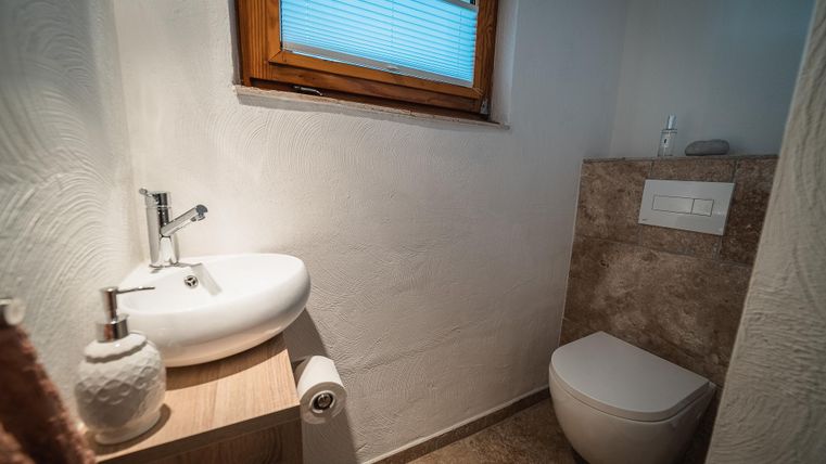 Ein modernes Badezimmer mit einem weißen Waschbecken und einer Toilette. Das Fenster lässt natürliches Licht hereinfliessen und sorgt für eine helle Atmosphäre.