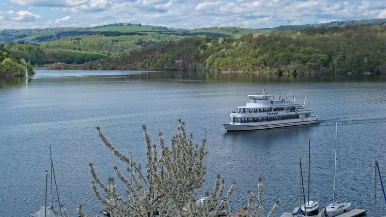 Ein ruhiger See mit einem Boot, das in der Mitte fährt. Im Hintergrund sind grüne Hügel und ein klarer Himmel zu sehen.