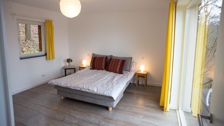 Ein helles Schlafzimmer mit einem großen Bett und bunten Kissen. Gelbe Vorhänge und sanfte Beleuchtung schaffen eine einladende Atmosphäre.