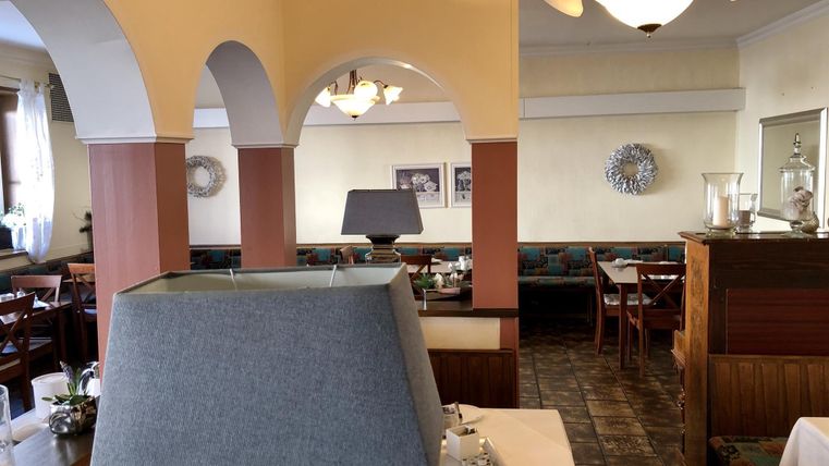 Ein gemütliches Restaurant mit einem einladenden Ambiente. Es gibt Tischlampen und Personen, die sich in einem hellen, freundlichen Raum entspannen.