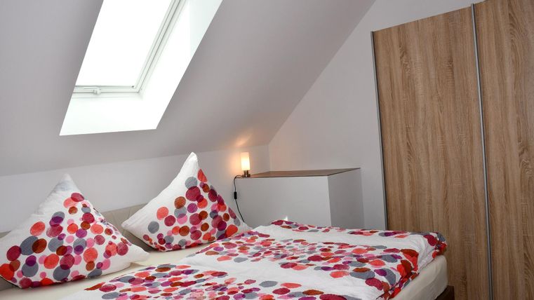 Ein gemütliches Schlafzimmer mit einem Doppelbett und bunten Kissen. Es gibt einen Kleiderschrank und ein Dachfenster, das Tageslicht hereinlässt.