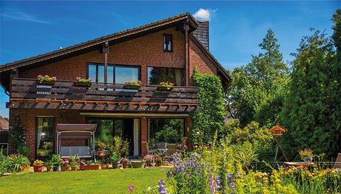 Ein einladendes Wohnzimmer mit Holzdecke und großen Fenstern. Es gibt bequeme Möbel, einen Esstisch und einen Kamin.