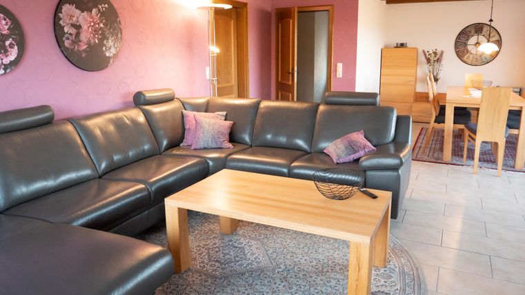 Ein modernes Wohnzimmer mit einer großen, bequemen Couch und einem Holztisch. Die Wände sind in einem sanften Rosa gehalten und dekorative Bilder schmücken den Raum.