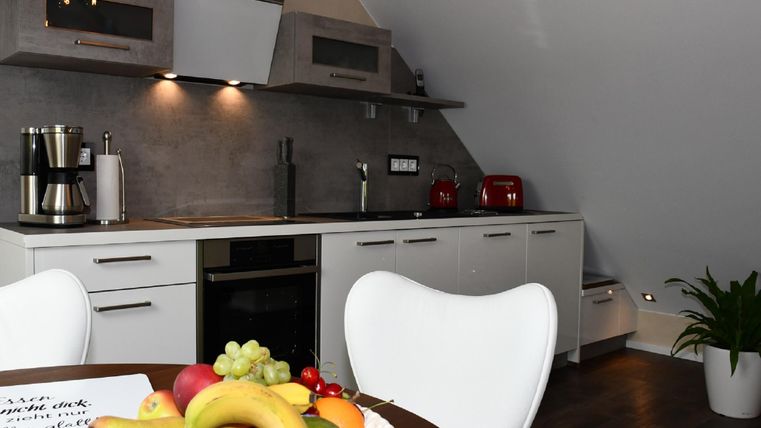 Eine moderne Küche mit weißen Schränken und einer eleganten Arbeitsplatte. Auf dem Tisch steht eine Obstschale mit verschiedenen Früchten.