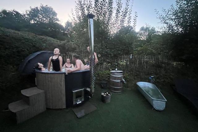 Eine Gruppe von Menschen entspannt in einem Whirlpool im Freien. Umgeben von grünen Bäumen und einem ruhigen Gartenambiente.