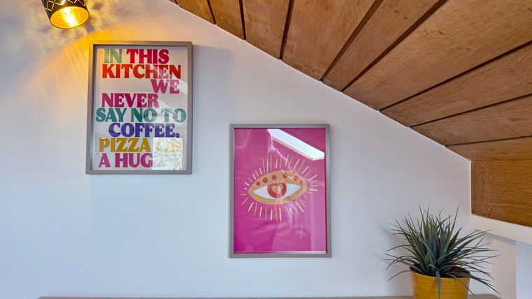 Ein gemütlicher Raum mit zwei bunten Bildern an der Wand. Im Vordergrund steht ein Topf mit einer Pflanze.