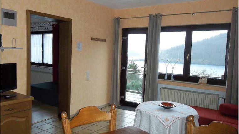 Ein gemütlicher Wohnraum mit einem Esstisch und einem Blick auf den See. Große Fenster lassen viel Licht herein und bieten eine Aussicht auf die umliegende Natur.