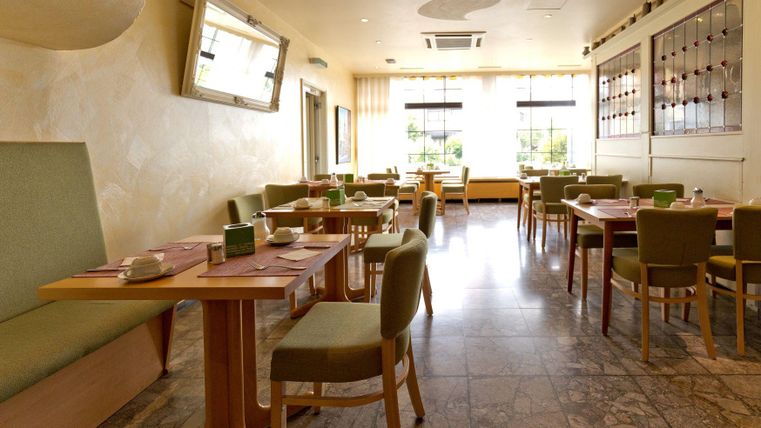 Ein modernes Restaurant mit hellen Wänden und eleganten Möbeln. Die Tische sind ordentlich gedeckt und es gibt viel natürliches Licht.
