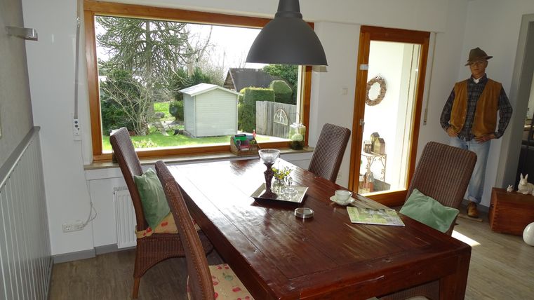 Ein gemütlicher Essbereich mit einem großen Holztisch und stimmungsvollem Licht. Durch die Fenster sieht man den Garten und ein kleines Gartenhaus.