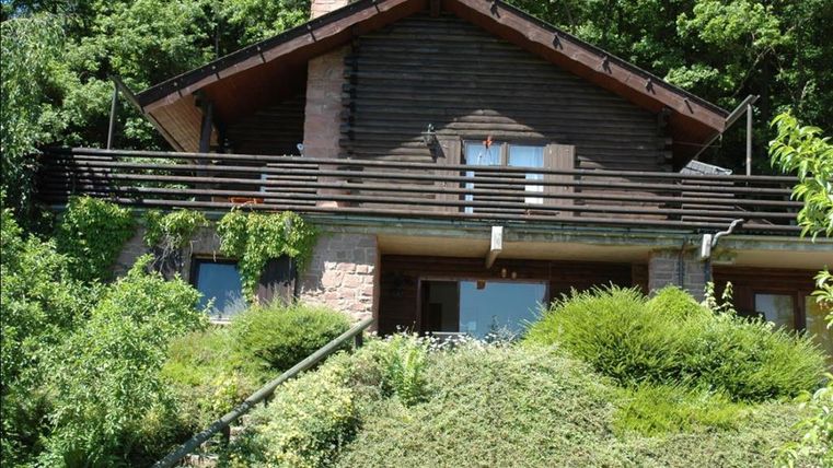 Ein schönes Holzhaus mit Balkon, umgeben von üppigem Grün. Der Garten und die Vegetation verleihen der Umgebung eine ruhige Atmosphäre.