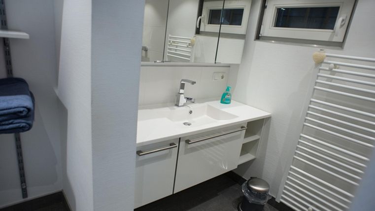 Ein modernes Badezimmer mit einem sauberen Waschbecken und großen Spiegeln. Handtücher sind ordentlich gestapelt und ein Heizkörper ist sichtbar.
