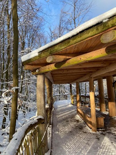 Eine Holzplattform im Schnee, umgeben von schneebedeckten Bäumen. Der Himmel ist klar und blau, was eine friedliche Atmosphäre schafft.