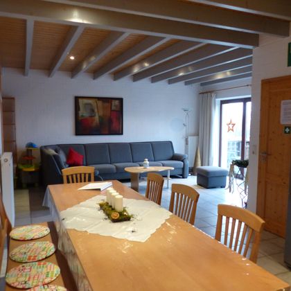 Eine moderne Küche mit einem großen Esstisch und Stühlen. Im Hintergrund befindet sich ein gemütliches Wohnzimmer mit einem Sofa und direktem Zugang zum Balkon.
